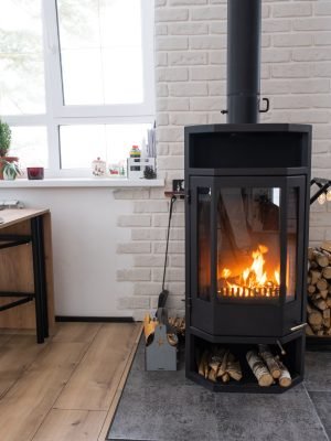 Interior festiu de casa decorat per Nadal i Any Nou en estil loft amb estufa negra, llar de foc, arbre de Nadal. Estudi càlid amb cuina blanca, llenya cremant, acollidor i calefacció de la llar
