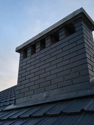 Chimney on house roof top covered with metallic shingles under construction. Tiled covering of building. Real estate development.